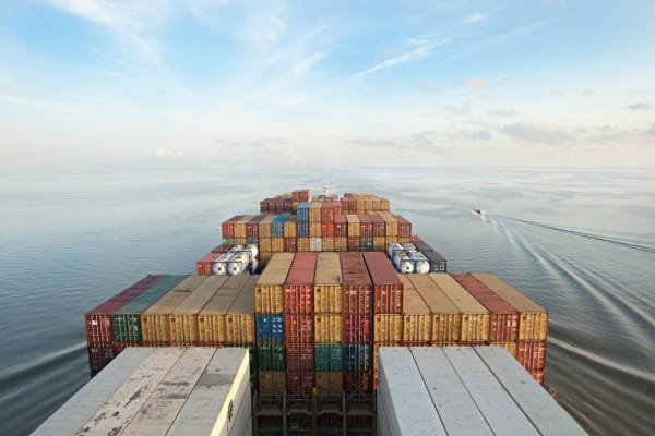 A barge of shipping containers floating on water is centered in the frame..